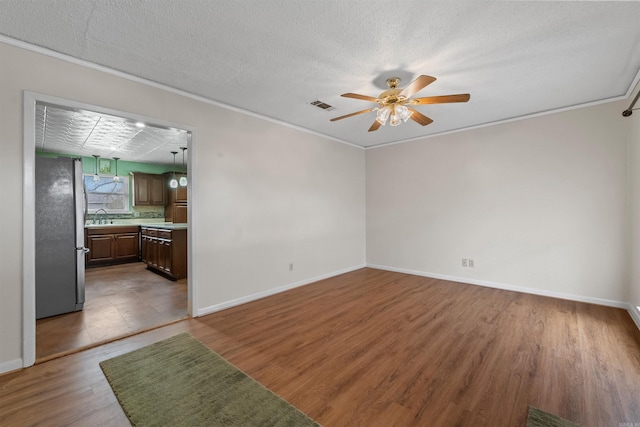 unfurnished living room featuring ceiling fan, a sink, wood finished floors, visible vents, and ornamental molding