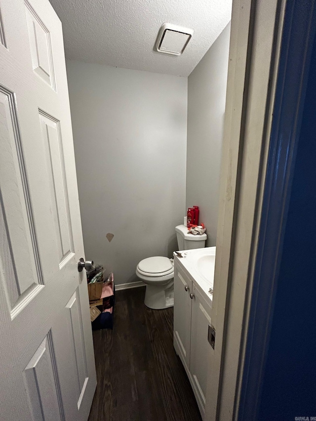 half bathroom featuring baseboards, toilet, wood finished floors, a textured ceiling, and vanity