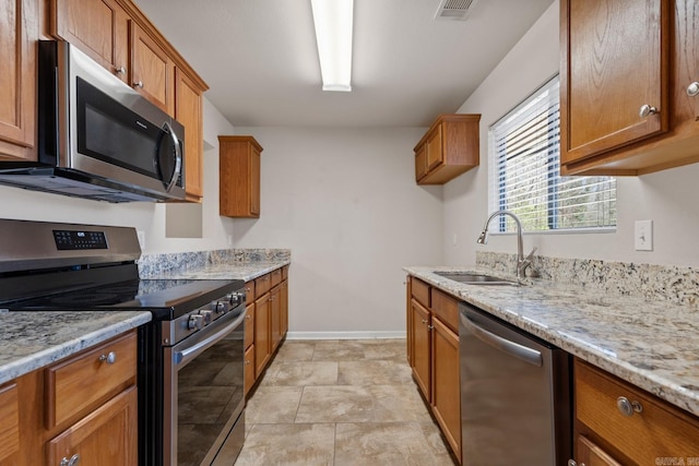 kitchen with light stone counters, visible vents, appliances with stainless steel finishes, brown cabinetry, and a sink