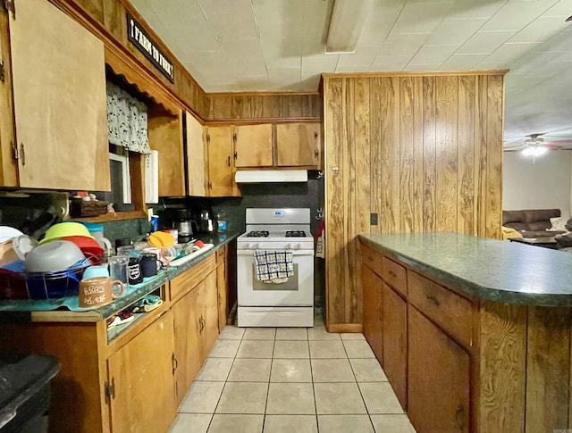 kitchen with light tile patterned floors, white gas range, ceiling fan, a peninsula, and under cabinet range hood