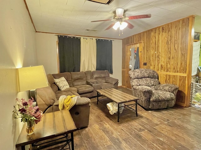 living room with crown molding, wooden walls, a ceiling fan, and wood finished floors