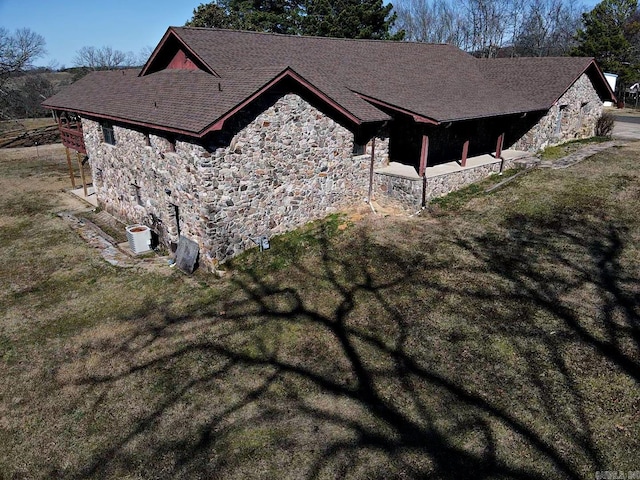 view of side of home featuring a shingled roof, stone siding, central AC, and a lawn