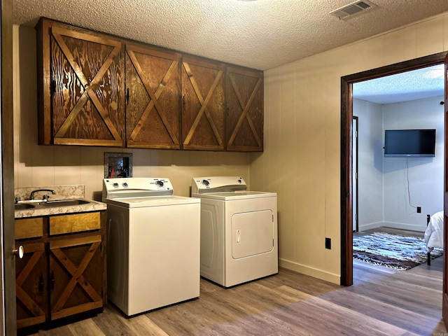 clothes washing area with a textured ceiling, separate washer and dryer, a sink, visible vents, and light wood-style floors