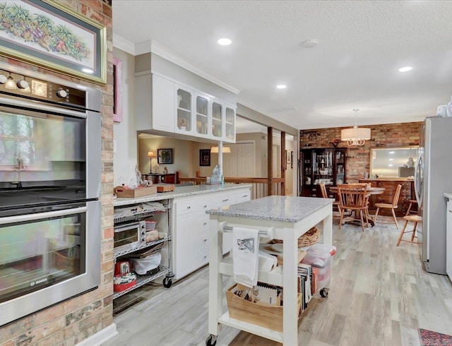 121 Chappel Hill Rd, Hot Springs, AR 71913 - kitchen with brick wall, white cabinets, light wood-style floors, and appliances with stainless steel finishes
