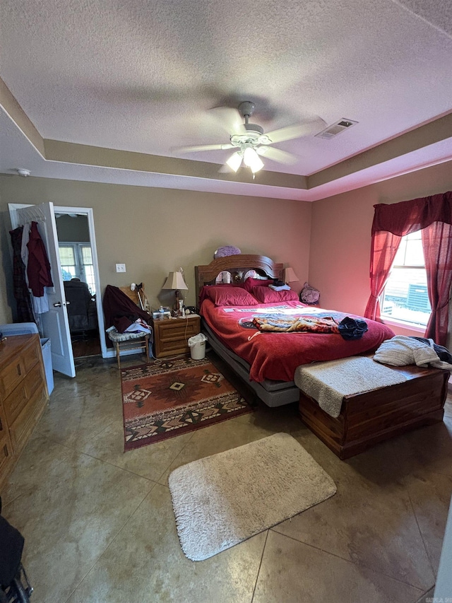 bedroom with a tray ceiling, visible vents, ceiling fan, and a textured ceiling