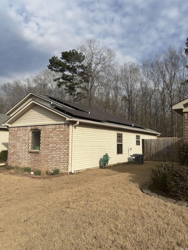 view of side of property with a lawn, solar panels, fence, central air condition unit, and brick siding