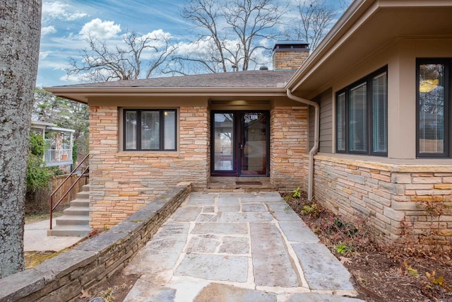 view of exterior entry featuring a shingled roof, stone siding, and a chimney