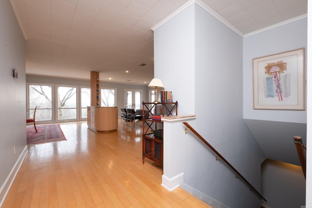 hallway with light wood-style floors, baseboards, crown molding, and an upstairs landing