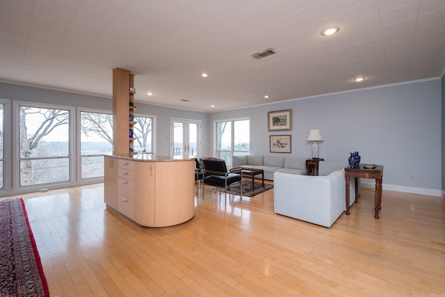 living room with light wood-style floors, visible vents, crown molding, and baseboards