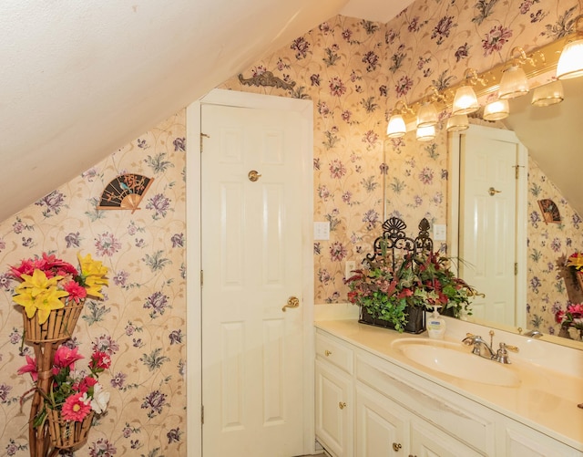 bathroom with wallpapered walls, vanity, and lofted ceiling