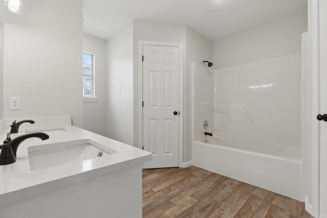 bathroom with double vanity, tub / shower combination, a sink, and wood finished floors