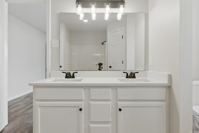 bathroom with wood finished floors, a sink, toilet, and double vanity