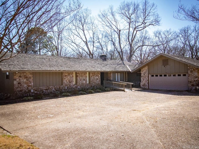 view of front facade with stone siding, an attached garage, and dirt driveway