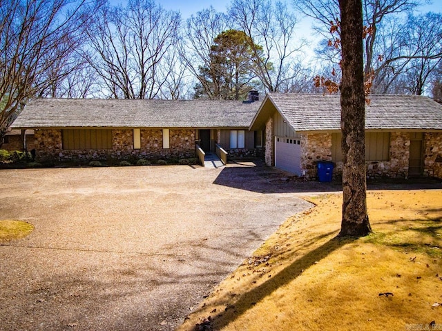 single story home featuring aphalt driveway, stone siding, board and batten siding, and an attached garage