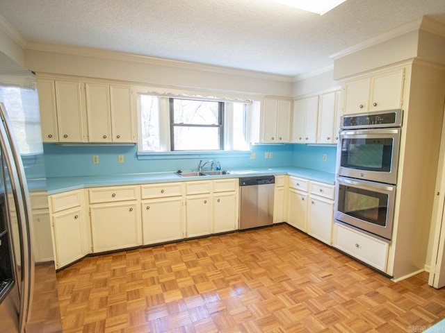 kitchen with stainless steel appliances, crown molding, a textured ceiling, light countertops, and a sink