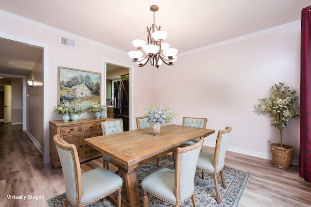 dining room featuring crown molding, visible vents, wood finished floors, a chandelier, and baseboards