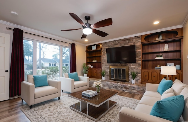 living room with built in shelves, ornamental molding, a ceiling fan, a brick fireplace, and wood finished floors