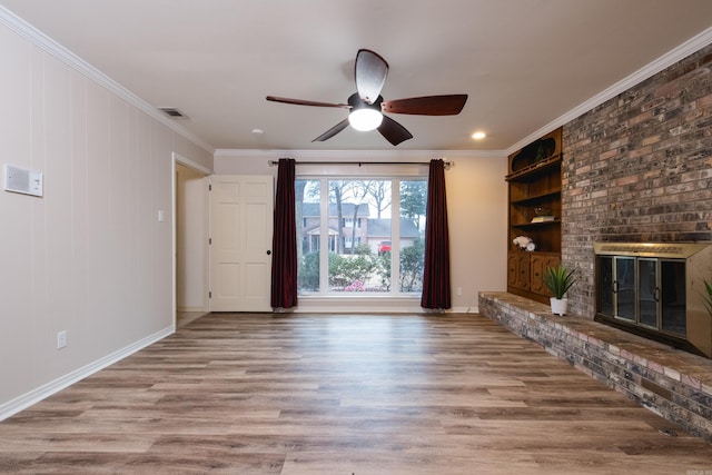 unfurnished living room featuring built in features, a brick fireplace, ornamental molding, and wood finished floors