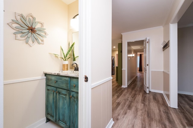 corridor with a sink, crown molding, wood finished floors, and wainscoting