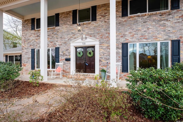 view of exterior entry featuring covered porch and brick siding