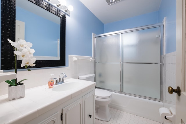 bathroom featuring bath / shower combo with glass door, toilet, tile patterned floors, vanity, and tile walls