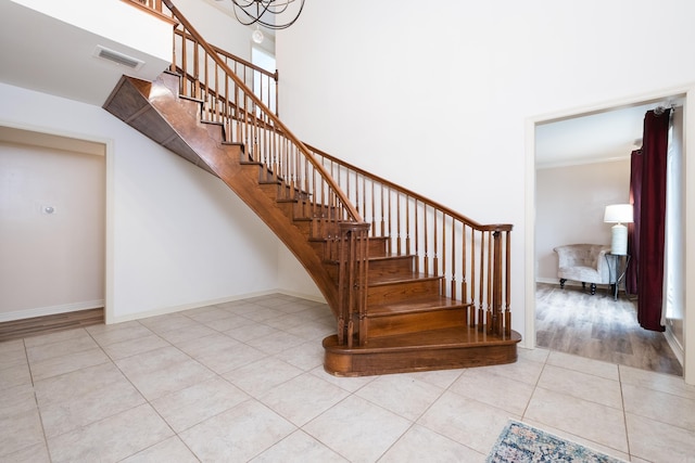 stairs with crown molding, visible vents, a high ceiling, tile patterned flooring, and baseboards