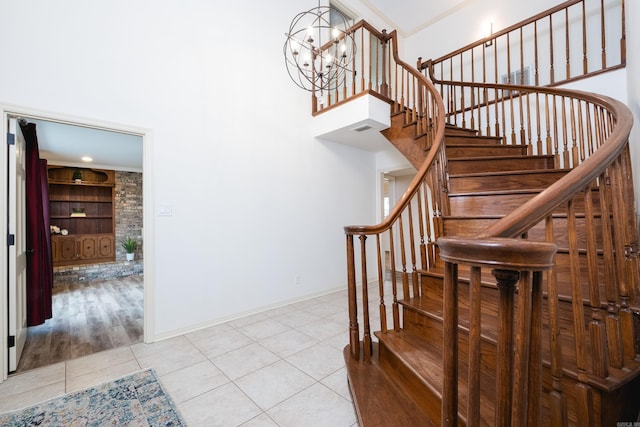 stairs featuring a notable chandelier, visible vents, a high ceiling, baseboards, and tile patterned floors