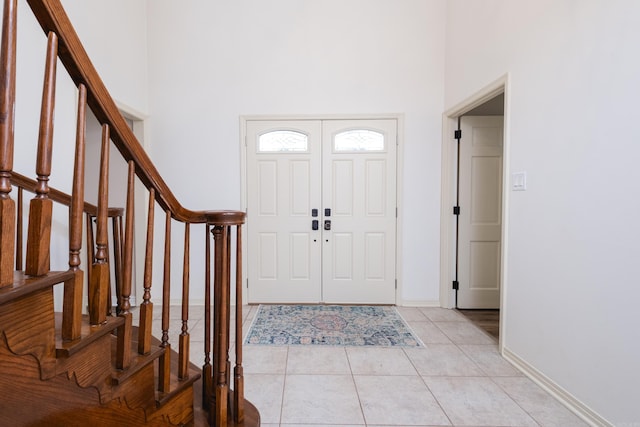 entrance foyer featuring a towering ceiling, light tile patterned floors, baseboards, and stairway