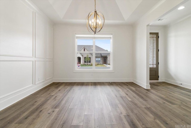 empty room with baseboards, recessed lighting, an inviting chandelier, wood finished floors, and a raised ceiling