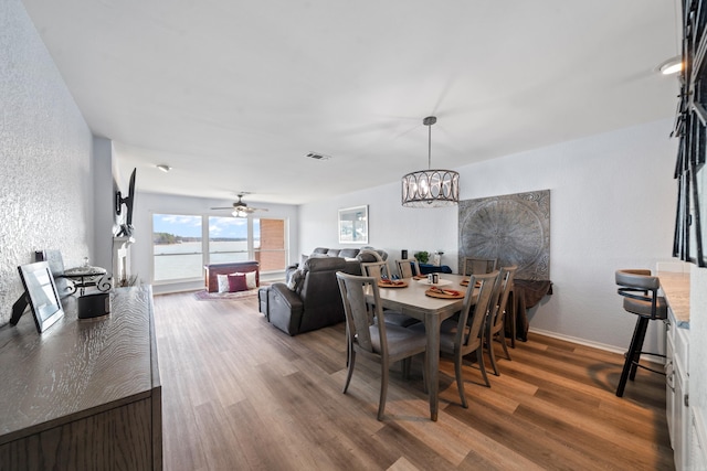 dining room featuring ceiling fan with notable chandelier, wood finished floors, visible vents, and baseboards