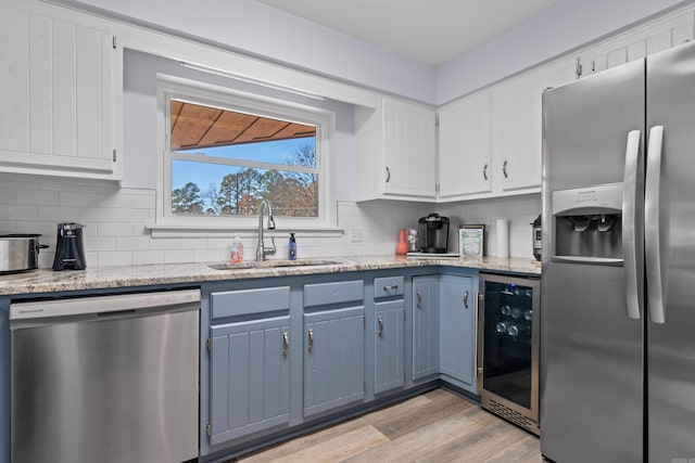 kitchen with white cabinets, wine cooler, appliances with stainless steel finishes, a sink, and backsplash