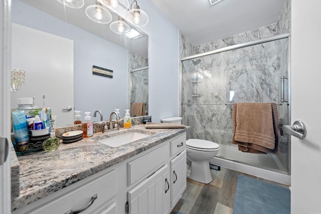 bathroom featuring toilet, a marble finish shower, wood finished floors, and vanity