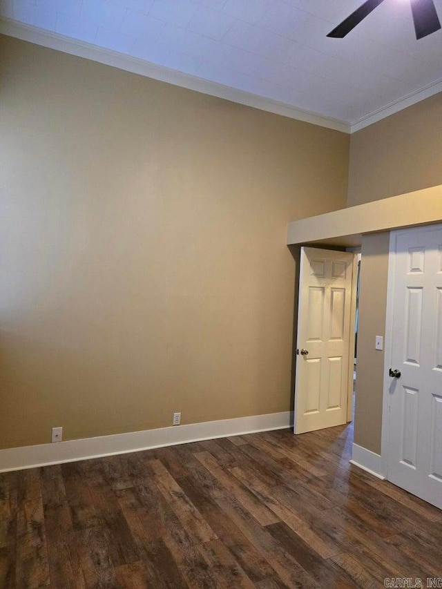 empty room featuring ornamental molding, dark wood finished floors, baseboards, and a ceiling fan