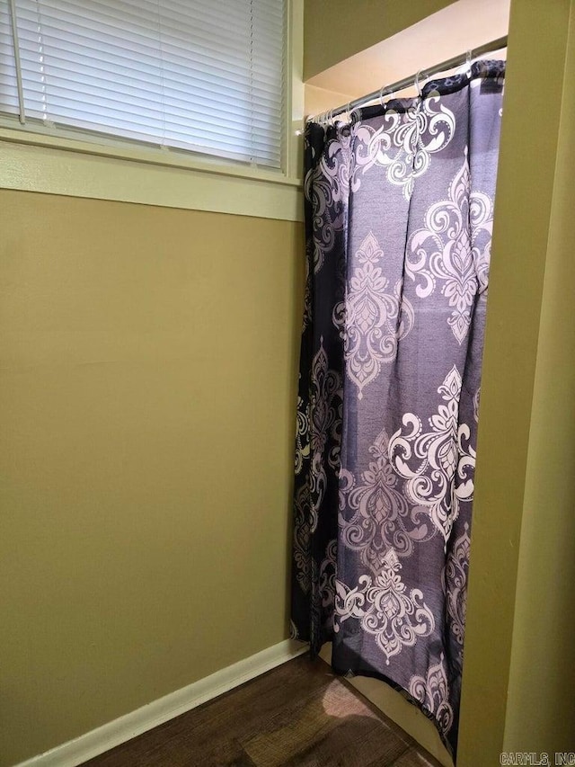 full bath featuring a shower with shower curtain, wood finished floors, and baseboards