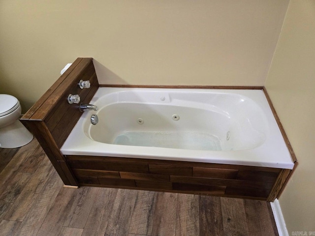 full bathroom featuring a whirlpool tub, toilet, and wood finished floors