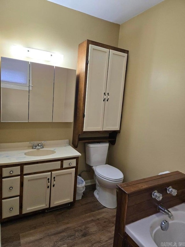 bathroom featuring toilet, a washtub, wood finished floors, and vanity