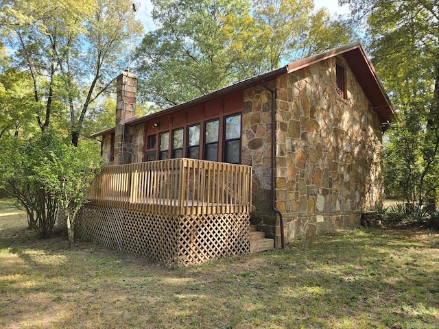 rear view of property with a deck, stone siding, a lawn, and a chimney