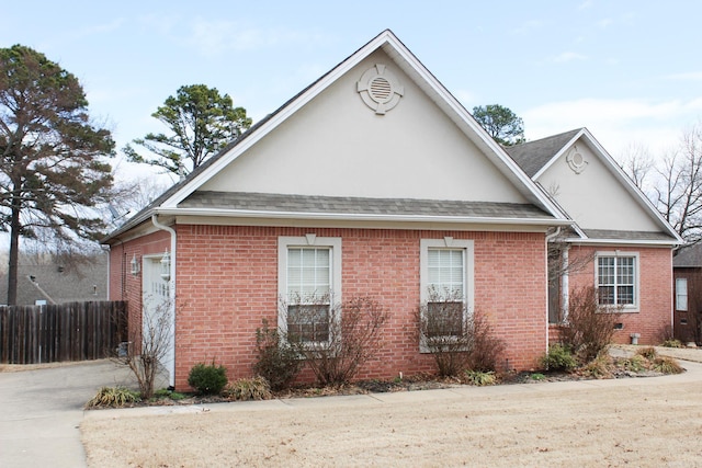 view of side of property with stucco siding, brick siding, fence, and roof with shingles