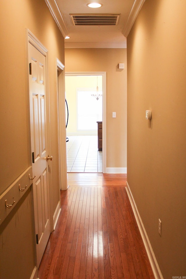 hallway with ornamental molding, visible vents, dark wood finished floors, and baseboards