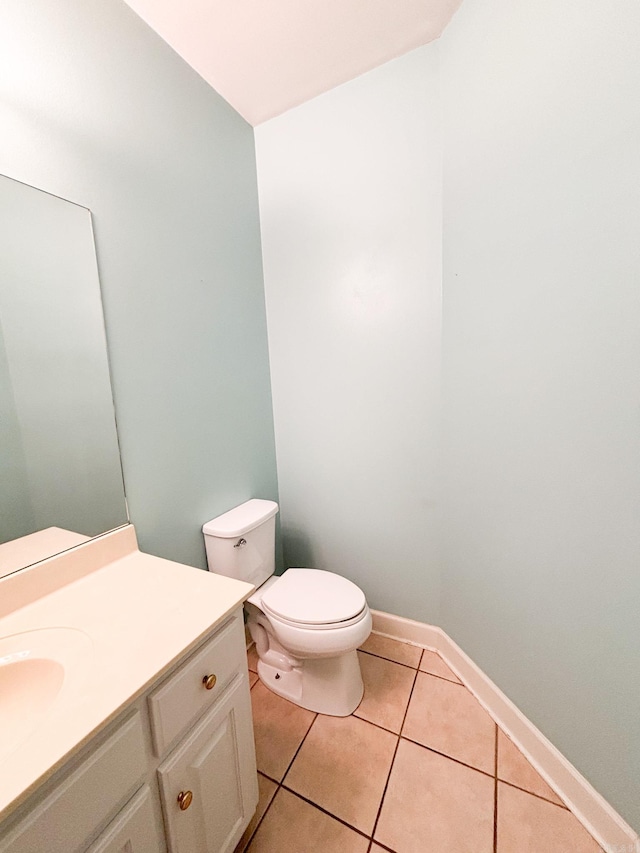 half bathroom with toilet, vanity, baseboards, and tile patterned floors