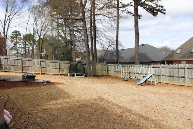 view of yard featuring a trampoline, a playground, and a fenced backyard