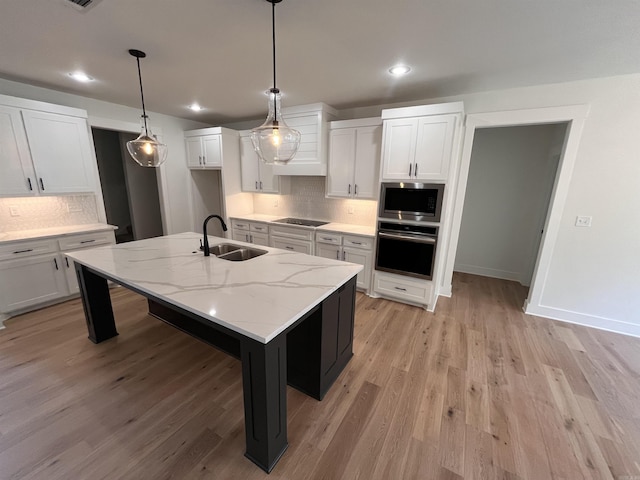 kitchen featuring stainless steel appliances, tasteful backsplash, white cabinets, a sink, and light wood-type flooring