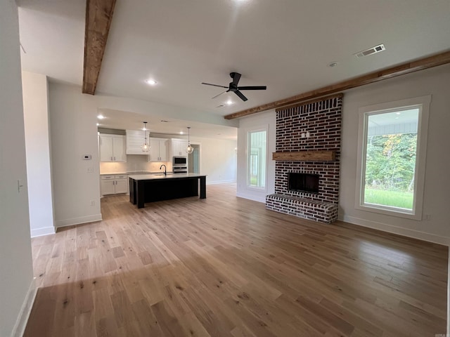 unfurnished living room with visible vents, baseboards, light wood-style floors, a brick fireplace, and beam ceiling