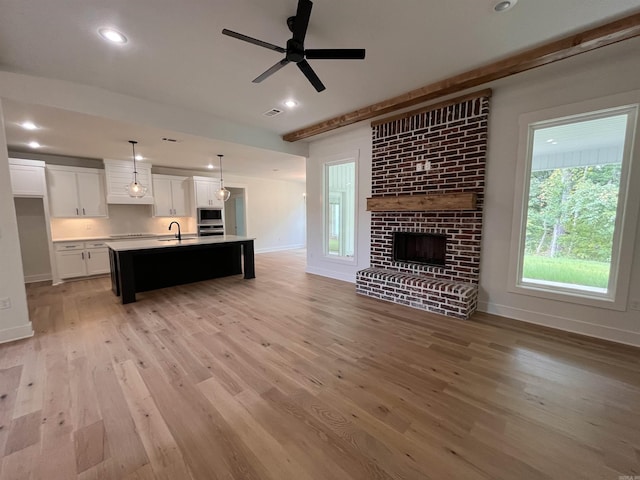 unfurnished living room featuring baseboards, light wood-style floors, a fireplace, a sink, and recessed lighting