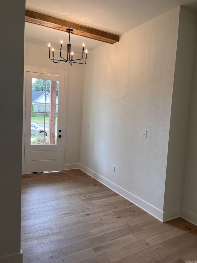 unfurnished dining area with baseboards, a chandelier, beam ceiling, and wood finished floors