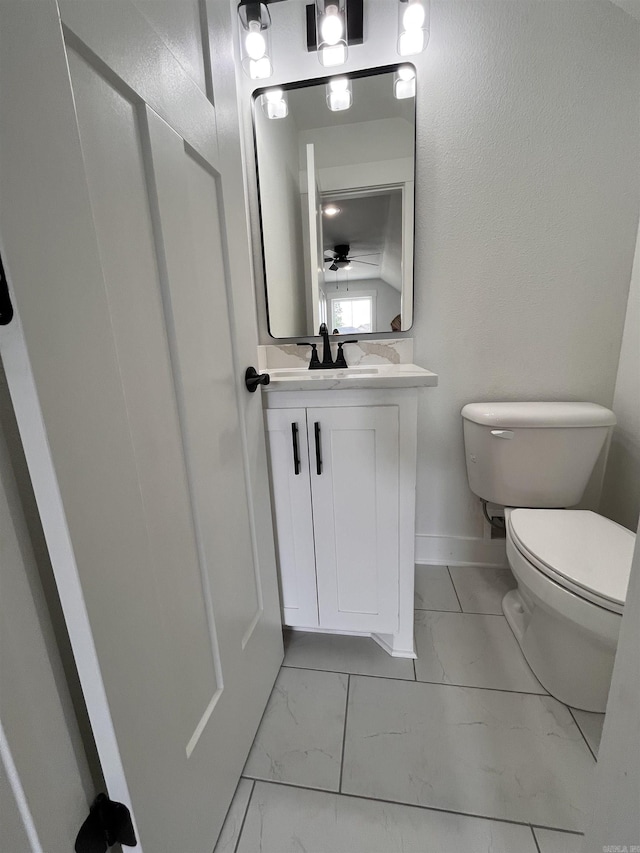 half bathroom featuring marble finish floor, baseboards, vanity, and toilet