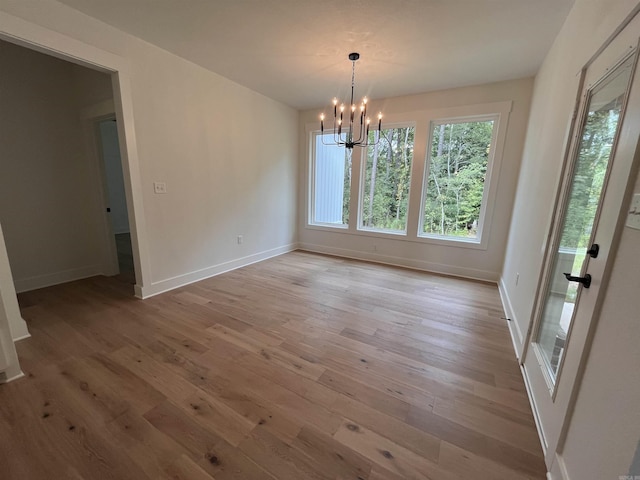 unfurnished dining area with a chandelier, baseboards, and light wood finished floors