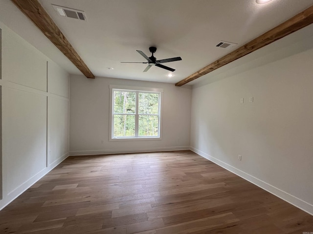 unfurnished room with visible vents, beamed ceiling, baseboards, and wood finished floors