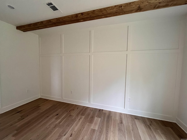 empty room with visible vents, a decorative wall, beamed ceiling, and wood finished floors