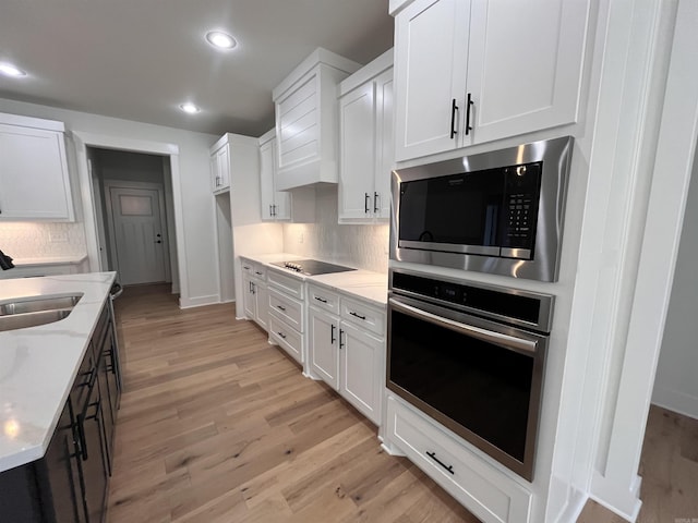 kitchen with light wood finished floors, white cabinets, stainless steel oven, a sink, and built in microwave